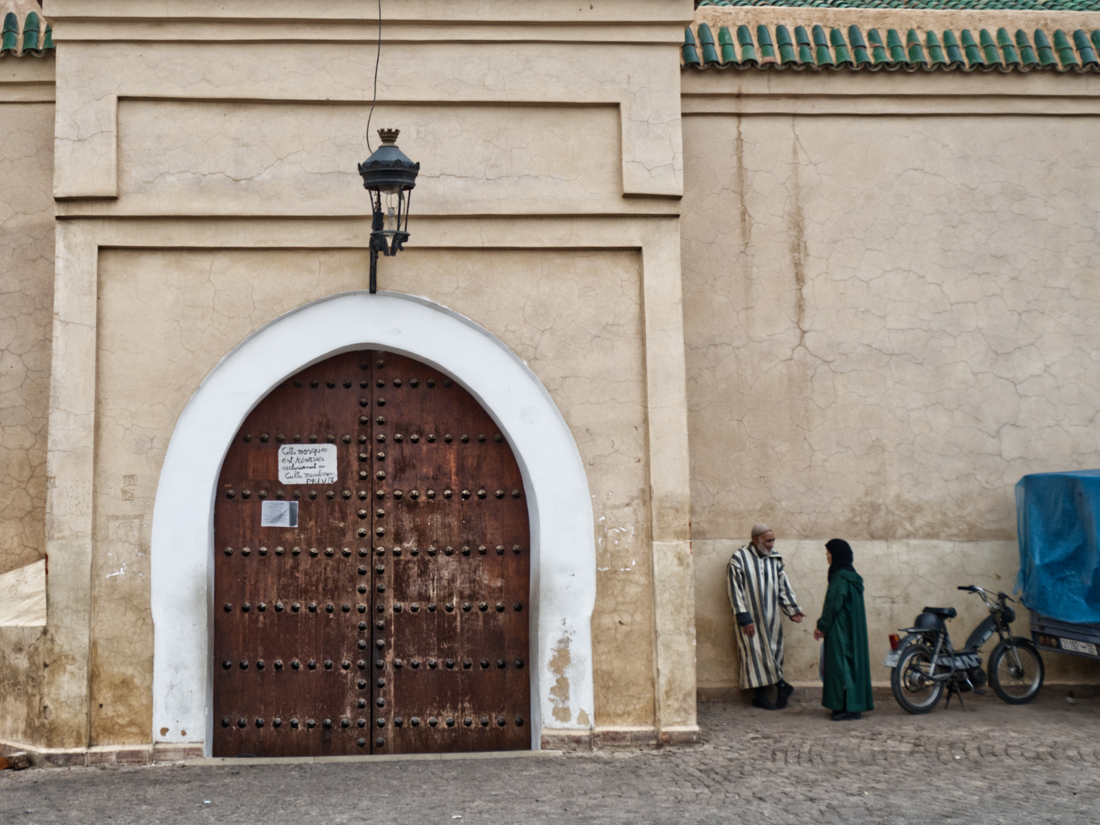 Locals talking outside the entrance to a mosque in Marrakech. The sign indicates that only Muslims are allowed to enter.