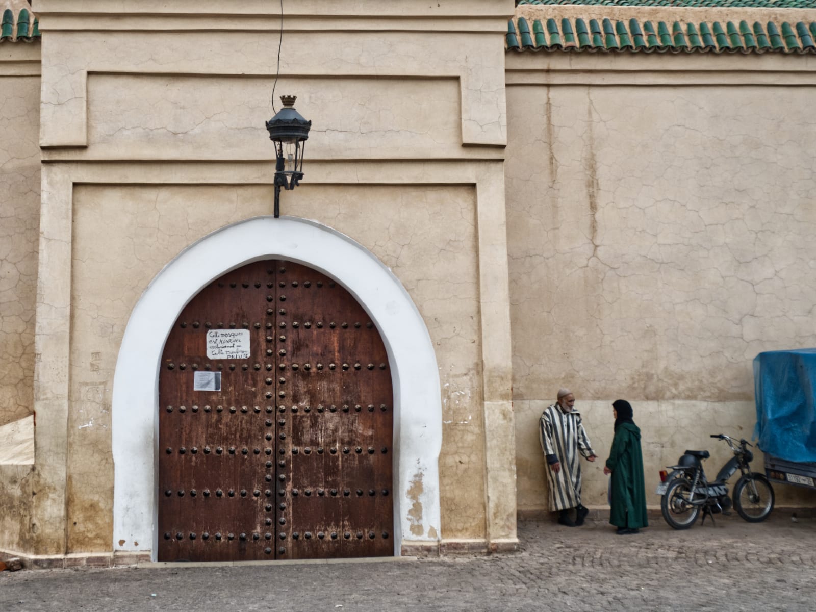 Locals talking outside the entrance to a mosque in Marrakech. The sign indicates that only Muslims are allowed to enter.
